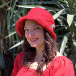 A white woman with brown curly hair wearing a red bucket hat and a red shirt.