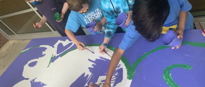 Three children with blue shirts working on a large purple mural.