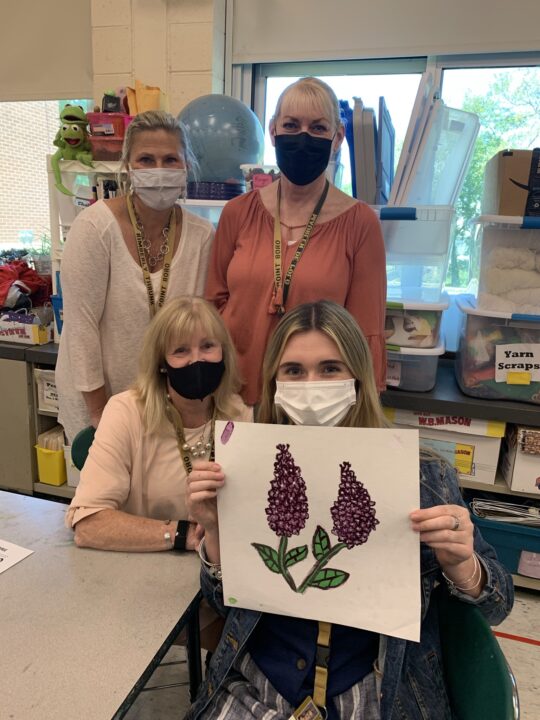 Four adult women holding a picture of a mosaic flower.